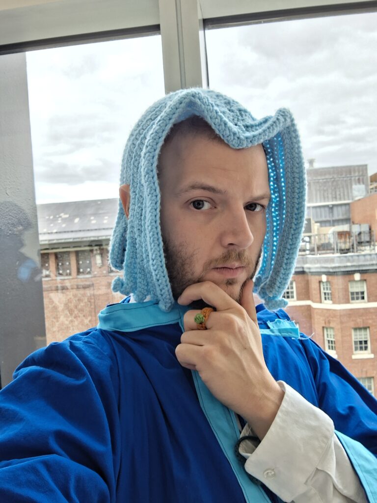 Ferdinand from Ascendance of a Bookworm close-up, head slightly to the side, looking at the camera. A ring is visible on the middle finger of the left hand.